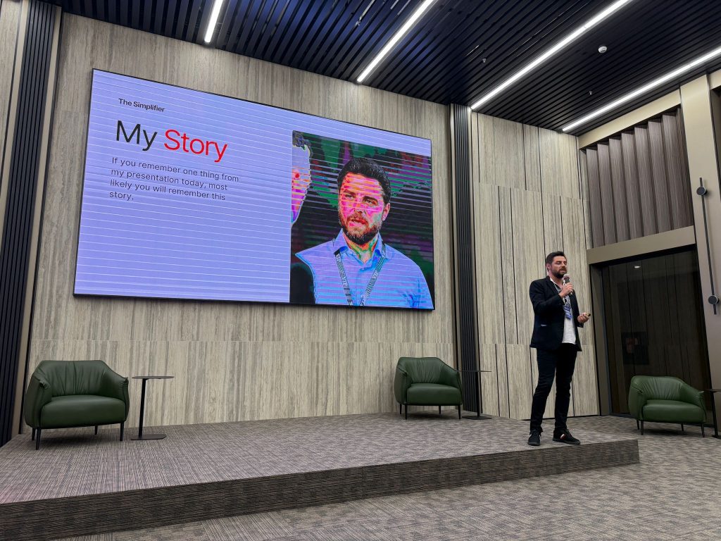Daniel Deaconu speaking at a tech conference on stage with presentation screen in background